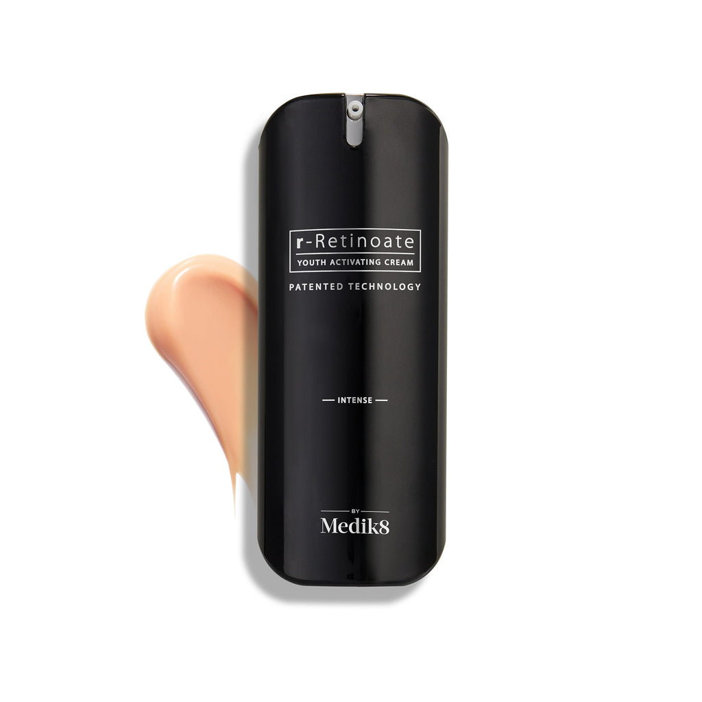 Een flacon Medik8 r-Retinoate Intense Youth Activating Cream gepresenteerd op een witte achtergrond, met daarachter een zichtbare veeg van de perzikkleurige crèmetextuur.