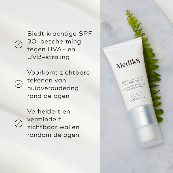 De tube Medik8 Advanced Day Eye Protect ligt op een marmeren oppervlak naast een groene varenblad. De tekst benadrukt de SPF 30-bescherming, het helpen voorkomen van zichtbare tekenen van huidveroudering en het vermogen om de oogcontour te verhelderen en wallen te verminderen.