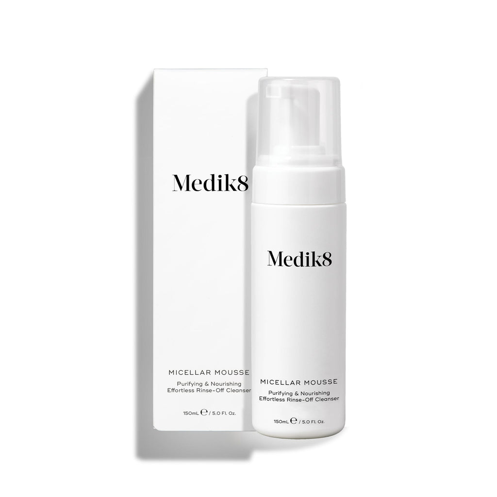 Een pompflacon van Medik8 Micellar Mousse naast de bijbehorende witte verpakking op een witte achtergrond. De tekst beschrijft het product als een zuiverende en voedende reiniger die gemakkelijk afspoelbaar is.
