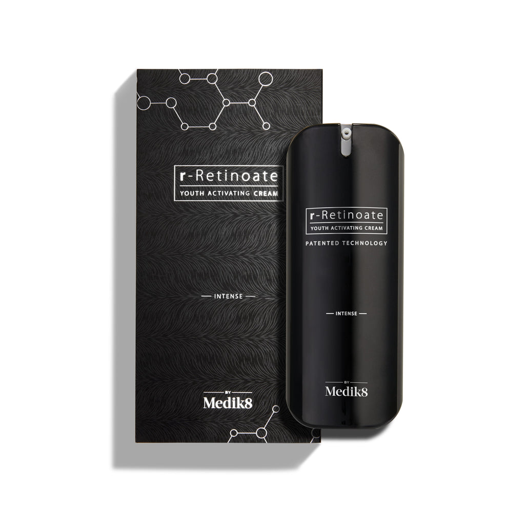 Een flacon Medik8 r-Retinoate Intense Youth Activating Cream staat naast de zwarte omverpakking, die is voorzien van witte zeshoekige graphics van chemische structuren en een golvend patroon met textuur.