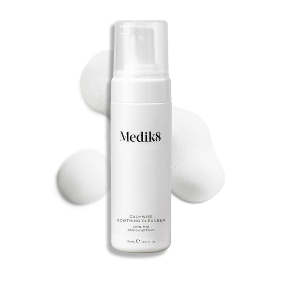 Een pompflacon Medik8 Calmwise Soothing Cleanser getoond op een witte achtergrond met een veeg wit schuim erachter om de textuur van het product te benadrukken.-4