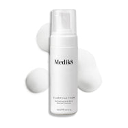 Een pompflacon Medik8 Clarifying Foam gepresenteerd op een strakke witte achtergrond met drie dotten wit, luchtig schuim. De tekst identificeert het product als een verfrissende AHA/BHA Blemish Cleanser met een inhoud van 150 ml.