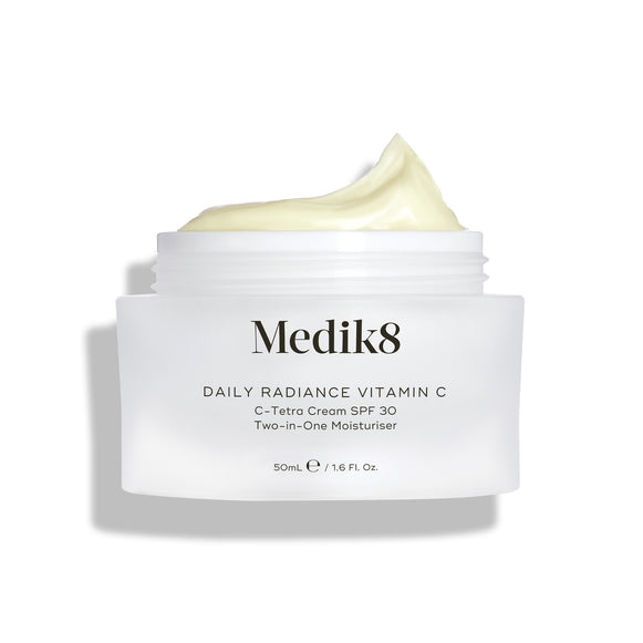 Een open glazen pot Medik8 Daily Radiance Vitamin C wordt getoond met een royale toef lichtgele crème bovenop. De tekst identificeert het product als een 50 ml C-Tetra Cream SPF 30, een twee-in-één moisturizer.-3