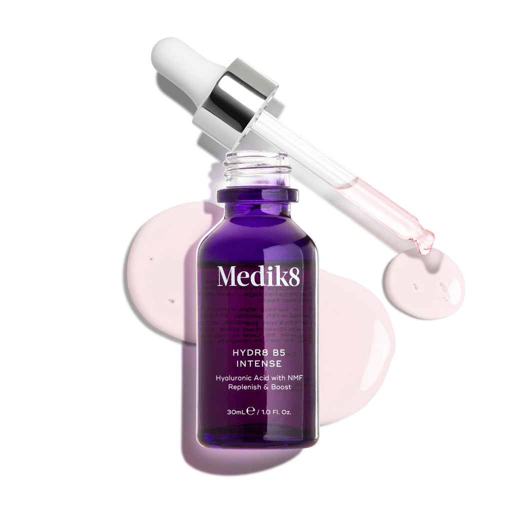 Een dieppaarse glazen Medik8 Hydr8 B5 Intense flacon met een open pipet die boven lichtroze serumdruppels rust op een strakke witte achtergrond. De tekst benadrukt de formule van 30 ml: Hyaluronzuur met NMF (Natural Moisturising Factors) om de huid aan te vullen en een boost te geven.