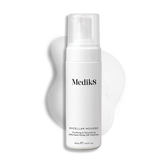 Een pompflacon Medik8 Micellar Mousse tegen een witte achtergrond met daarachter een veeg van wit schuim die de textuur van het product laat zien.-5