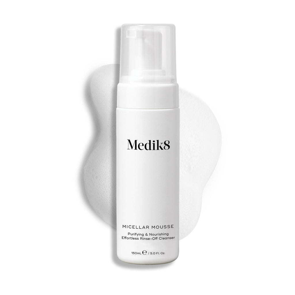 Een pompflacon Medik8 Micellar Mousse tegen een witte achtergrond met daarachter een veeg van wit schuim die de textuur van het product laat zien.
