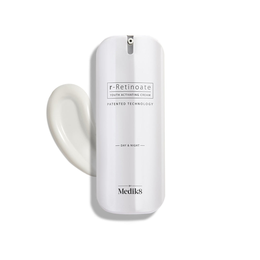 Een slanke witte pompflacon van r-Retinoate Day & Night staat rechtop, met daarnaast een sierlijke krul witte crème.