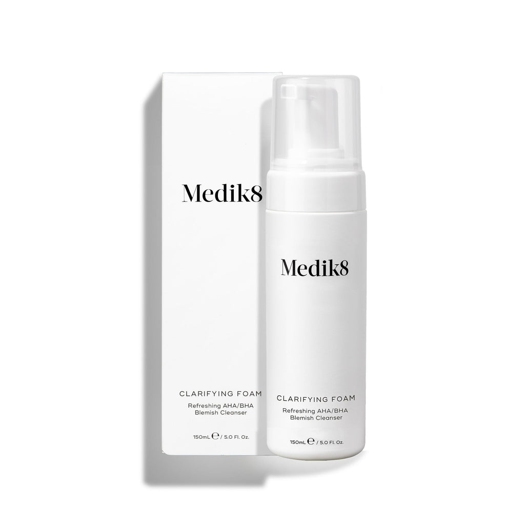 Een pompflacon Medik8 Clarifying Foam staat naast de bijbehorende witte omverpakking op een strakke witte achtergrond. De tekst op zowel de flacon als de doos identificeert het product als een Refreshing AHA/BHA Blemish Cleanser met een inhoud van 150 ml.