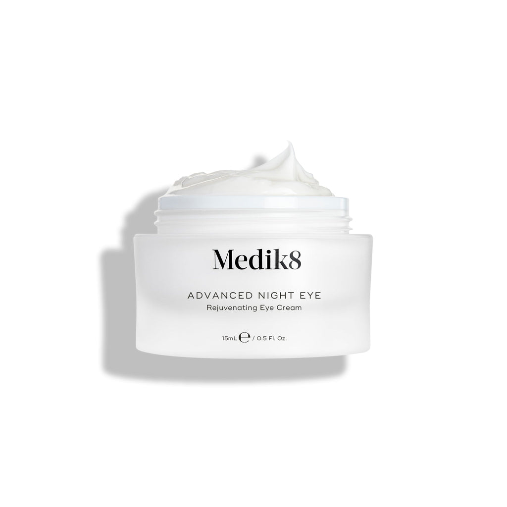 De pot met Medik8 Advanced Night Eye Cream staat tegen een witte achtergrond, met het deksel verwijderd. De rijke witte crème is zichtbaar in de pot en benadrukt de romige textuur.