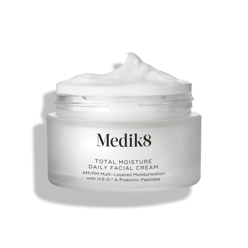 Een open, matglazen pot van Medik8 Total Moisture Daily Facial Cream met een toef witte crème bovenop, geplaatst tegen een strakke witte achtergrond.