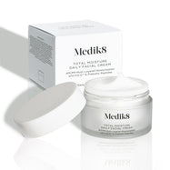 Een open, matglazen pot van Medik8 Total Moisture Daily Facial Cream met een witte deksel ernaast, waarbij de rijke witte crème zichtbaar is. De pot staat voor de witte kartonnen verpakking op een lichte achtergrond.