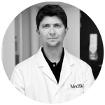 Een zwart-witportret van een Medik8-huidverzorgingswetenschapper en oprichter, gekleed in een labjas met merklogo, dat het onderzoek en de innovatie achter de formulering vertegenwoordigt.