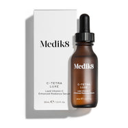 Een flesje Medik8 C-Tetra Luxe serum en de bijbehorende witte kartonnen verpakking op een strakke witte achtergrond met zachte schaduwen. Het amberkleurige glazen flesje en de witte doos dragen beide het Medik8-logo en identificeren het product als C-TETRA LUXE Lipid Vitamin C Enhanced Radiance Serum in een formaat van 30 ml.