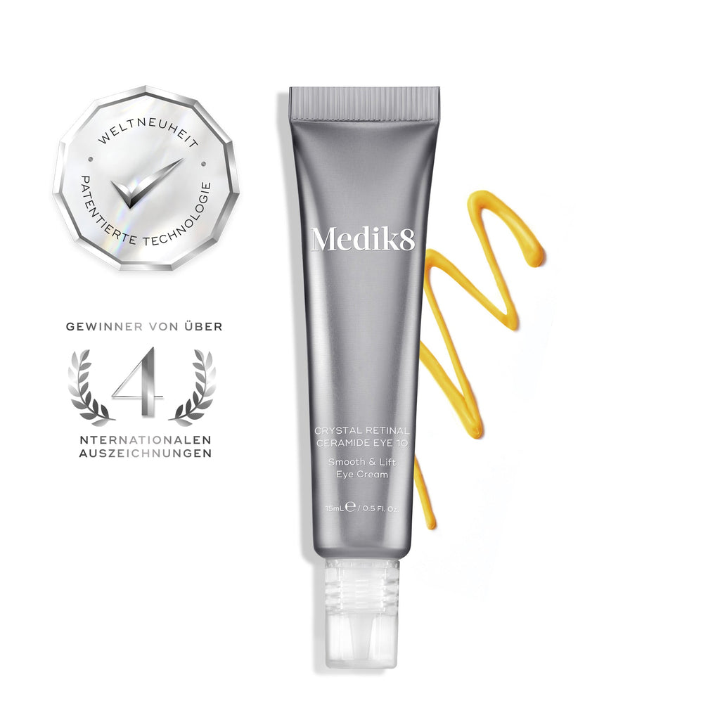 Een zilveren tube Crystal Retinal Ceramide Eye 10 staat rechtop, met daarnaast een swirl van geel-oranje crème aan de rechterkant.