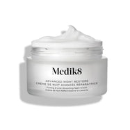 De geopende pot Medik8 Advanced Night Restore toont een rijke toef witte crème met een zachte piek tegen een strakke witte achtergrond, waardoor de gladde, herstellende textuur wordt benadrukt. De zwarte tekst op de pot luidt: "Rejuvenating Multi-Ceramide Night Cream."